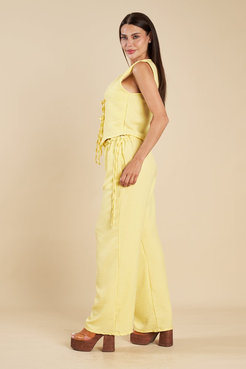 Modelo de corpo inteiro em conjunto amarelo de colete com amarração e calça larga, com sandália plataforma marrom