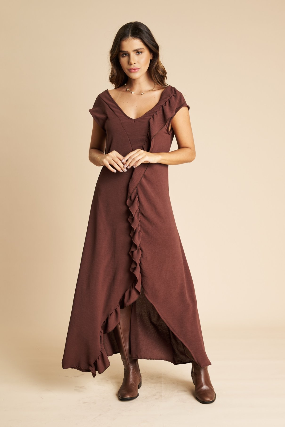 Modelo de vestido longo marrom chocolate com babado frontal, cinto de pedras e bota de cano alto marrom