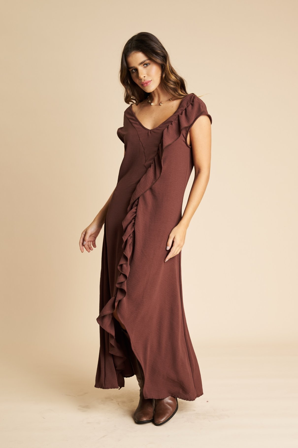 Vestido longo marrom fotografado de frente, mostrando o babado vertical e a saia ampla com barra assimétrica