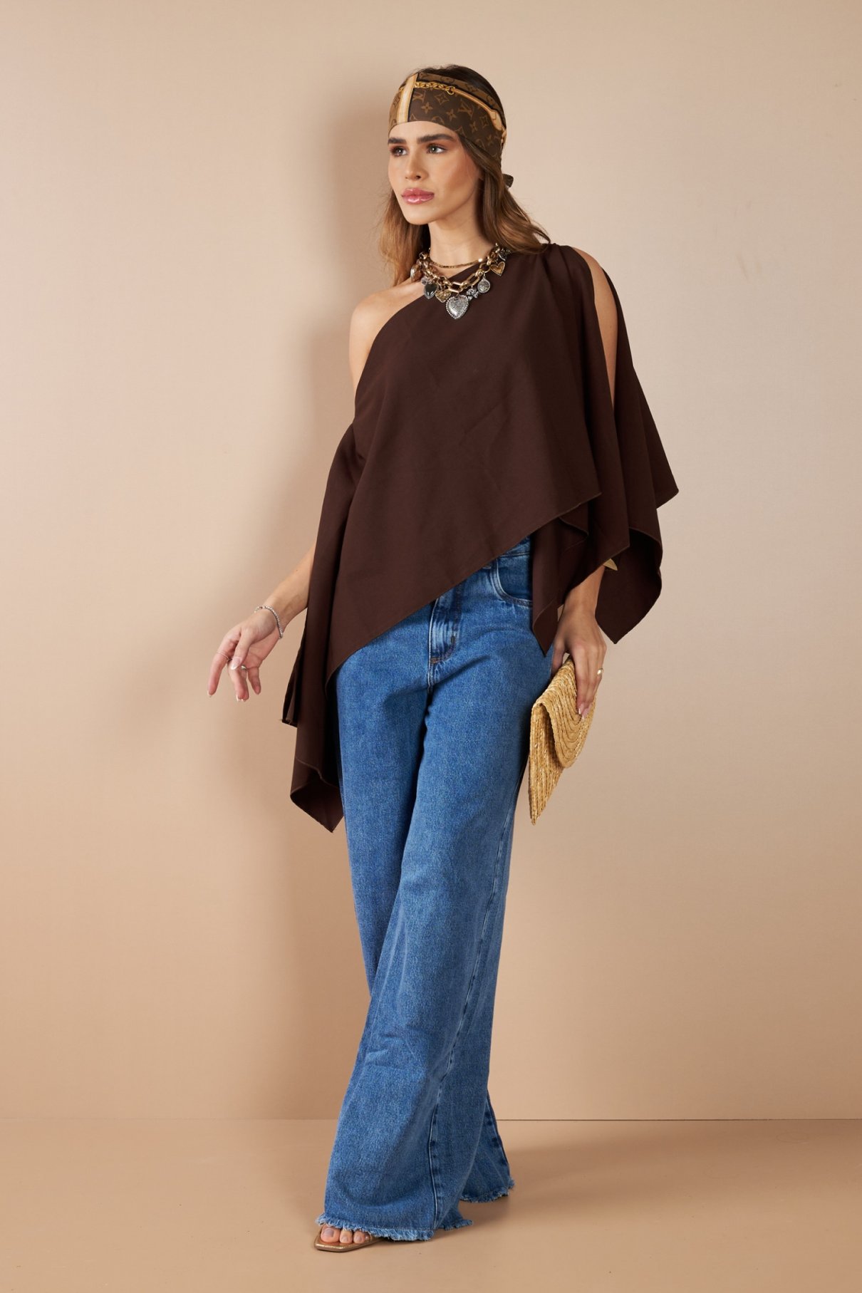 Poncho marrom assimétrico visto de corpo inteiro com calça jeans de perna ampla.