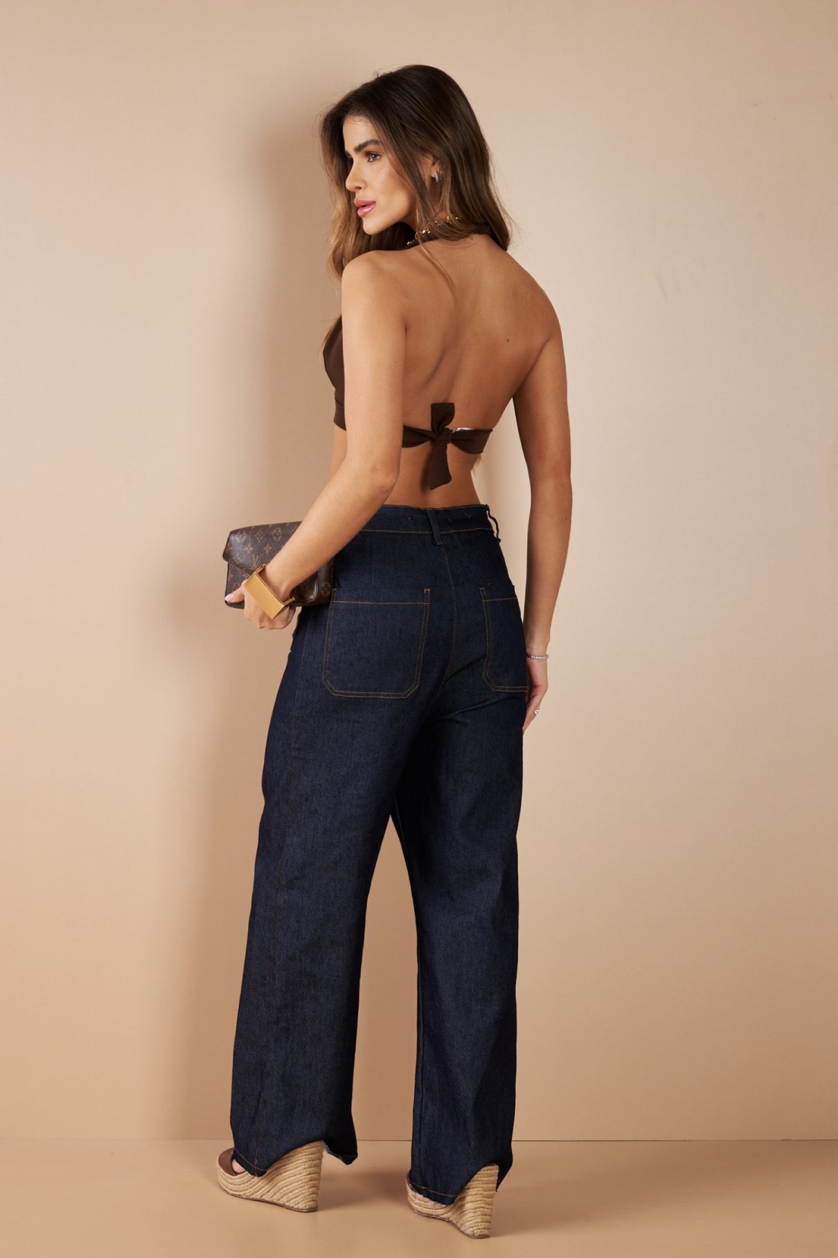 Modelo de corpo inteiro com top marrom de frente única e calça jeans escura de cintura alta e boca larga