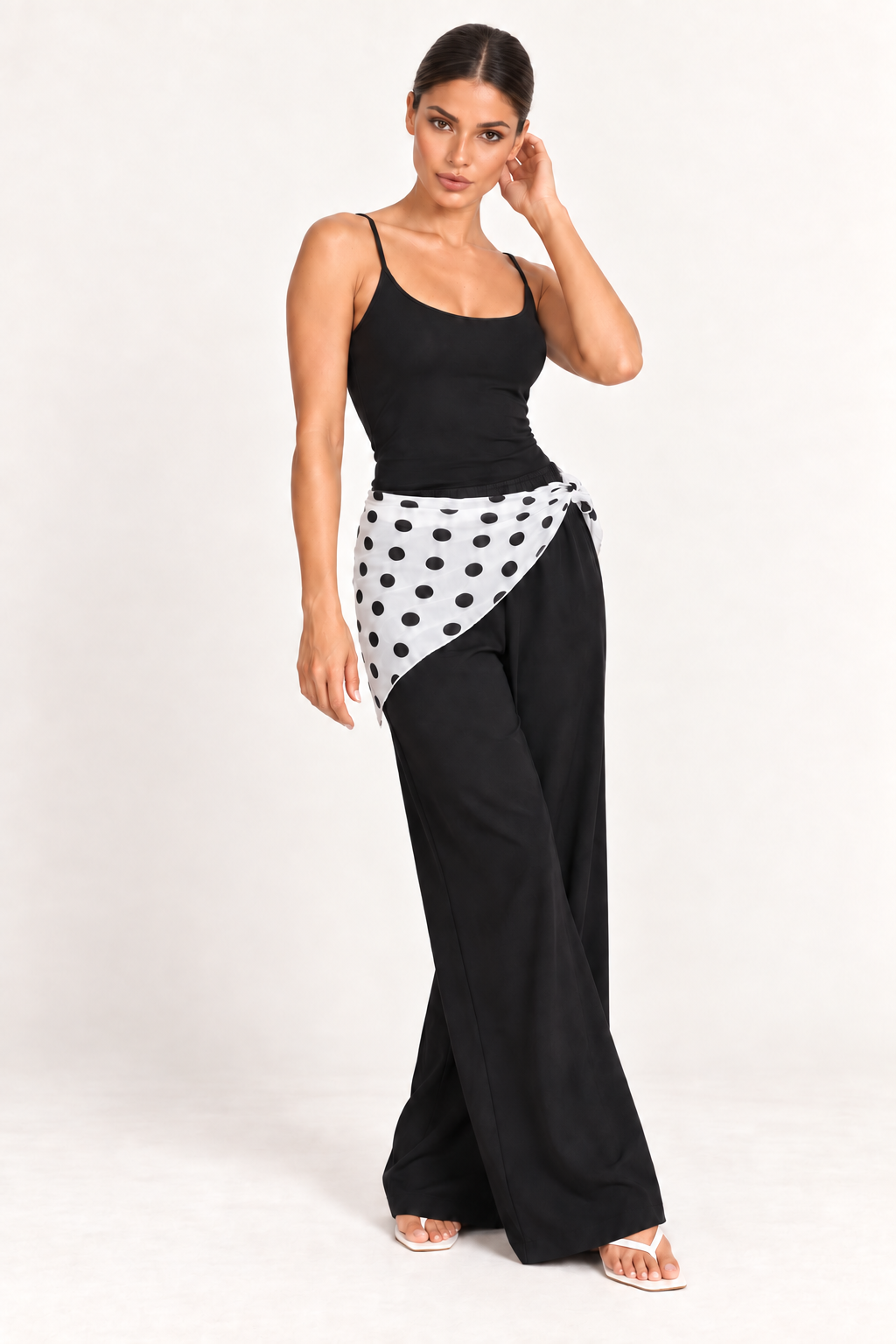 Mulher com lenço branco de poá preto amarrado na cintura, sobre blusa preta e calça pantalona preta.