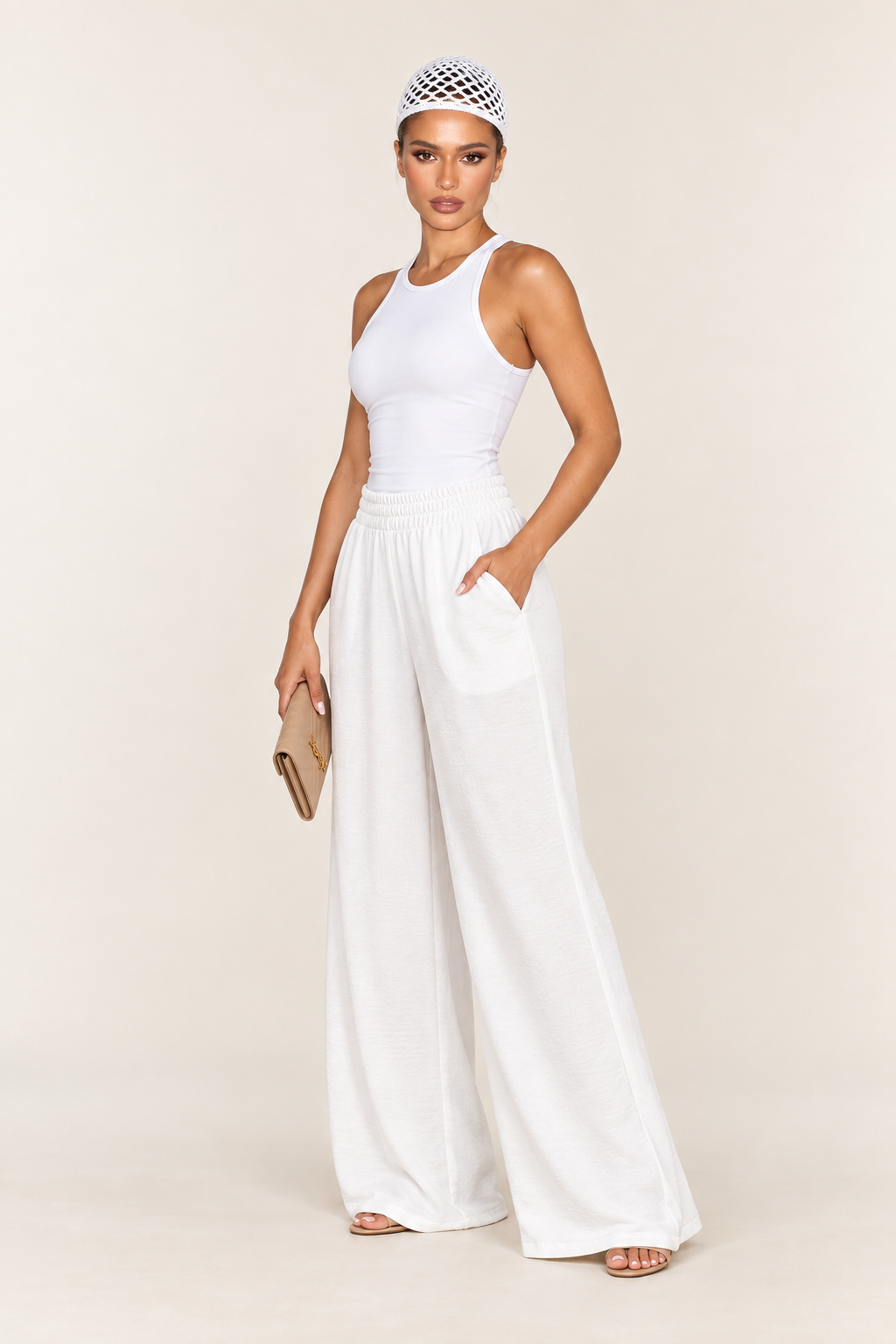 Modelo de blusa branca veste a calça pantalona off white com a mão no bolso lateral e segura uma carteira bege