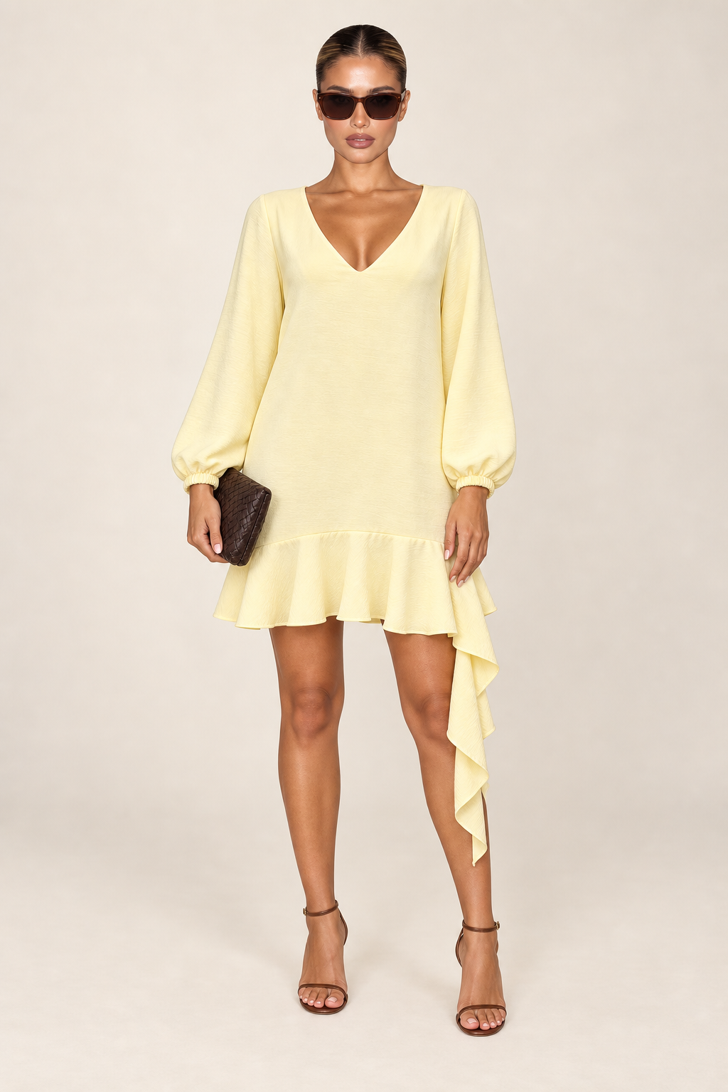 Vestido curto amarelo manteiga fotografado sozinho em fundo claro, com decote em V, manga bufante e babado assimétrico na barra
