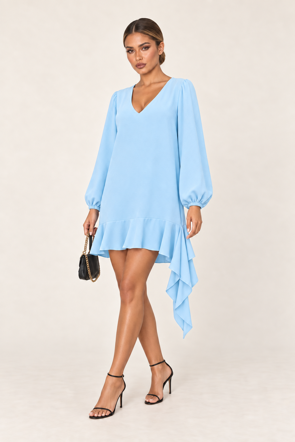 Modelo usa o vestido azul bebê, com a mão no rosto, mostrando o decote em V, o punho franzido e o babado rodado na barra